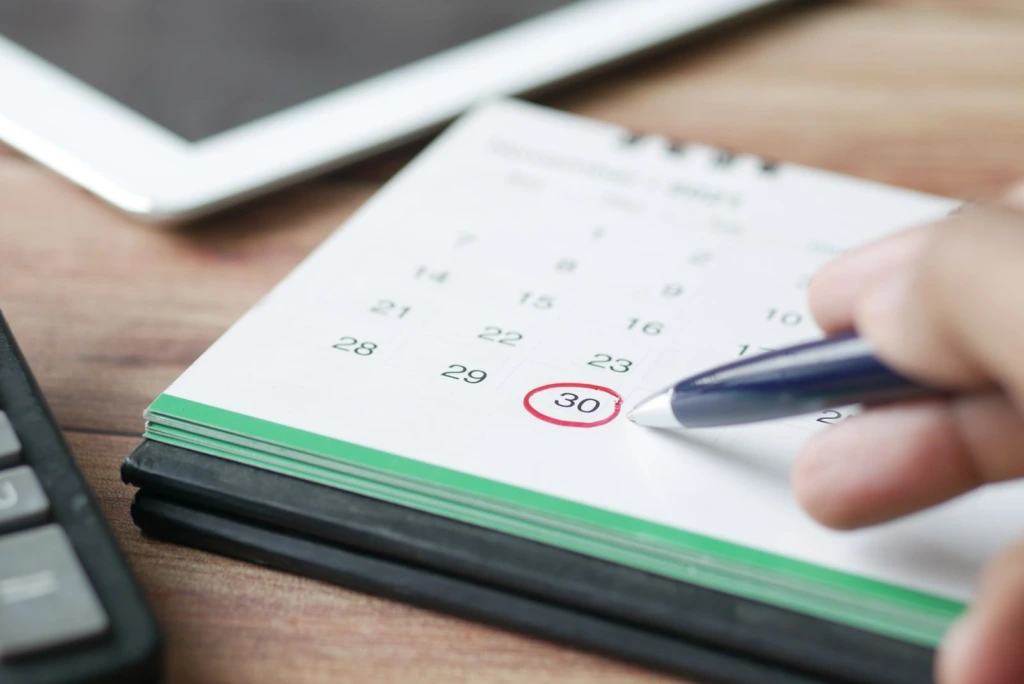Mano marcando una fecha en un calendario de escritorio con una pluma