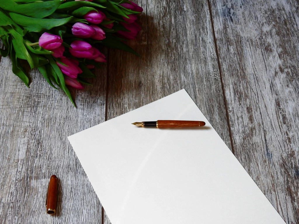 Hoja en blanco con una pluma fuente y tulipanes sobre una mesa de madera, lista para redactar una esquela de fallecimiento