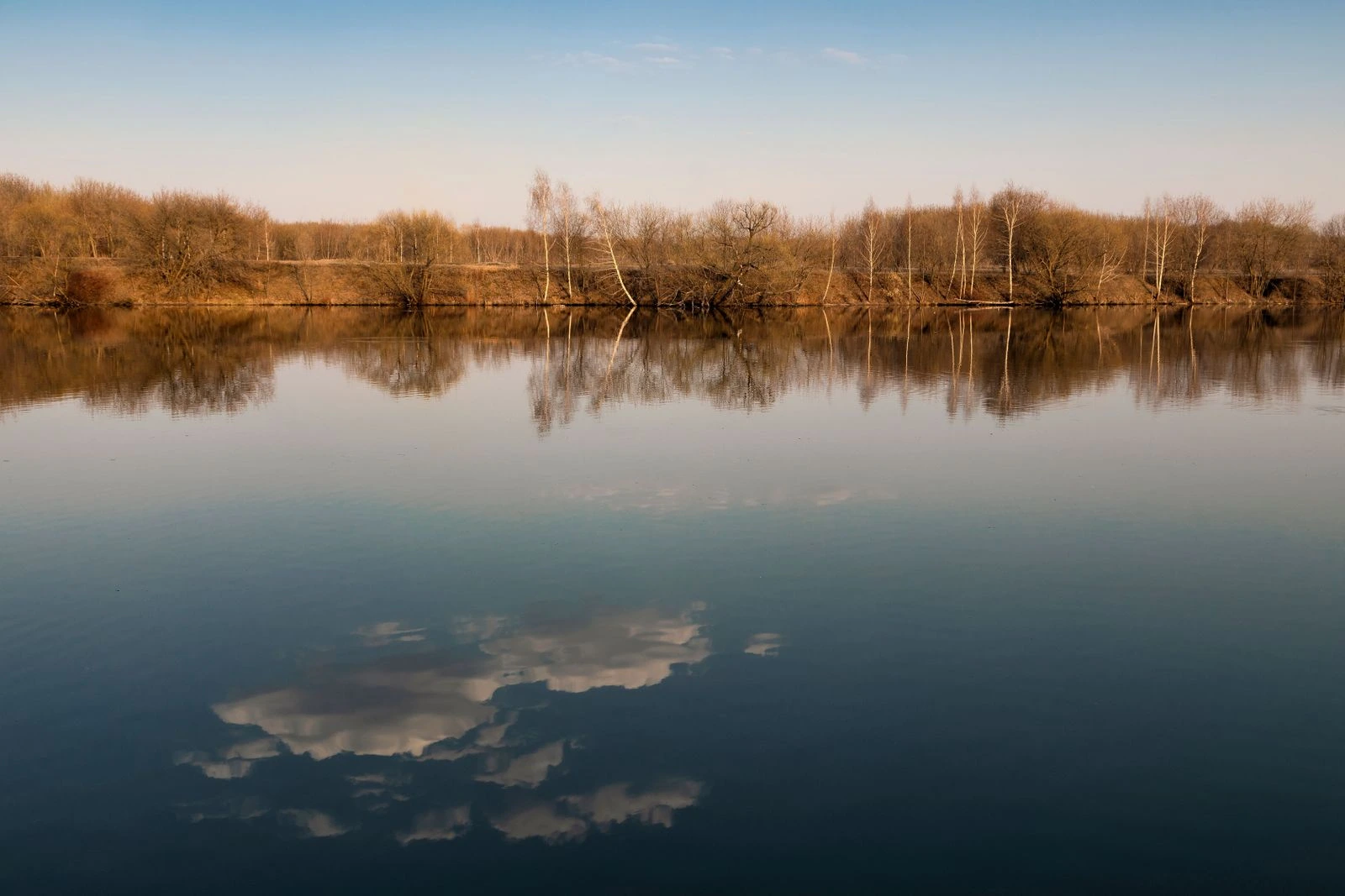 Lago en calma reflejando los árboles y las nubes, en referencia a las aguas de reposo del Salmo 23