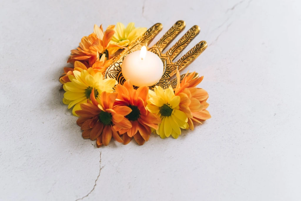Vela encendida rodeada de flores amarillas y naranjas sobre fondo blanco