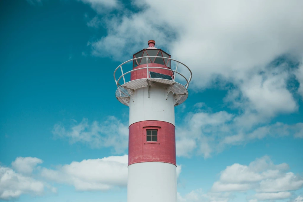 Faro blanco y rojo bajo un cielo azul con nubes blancas