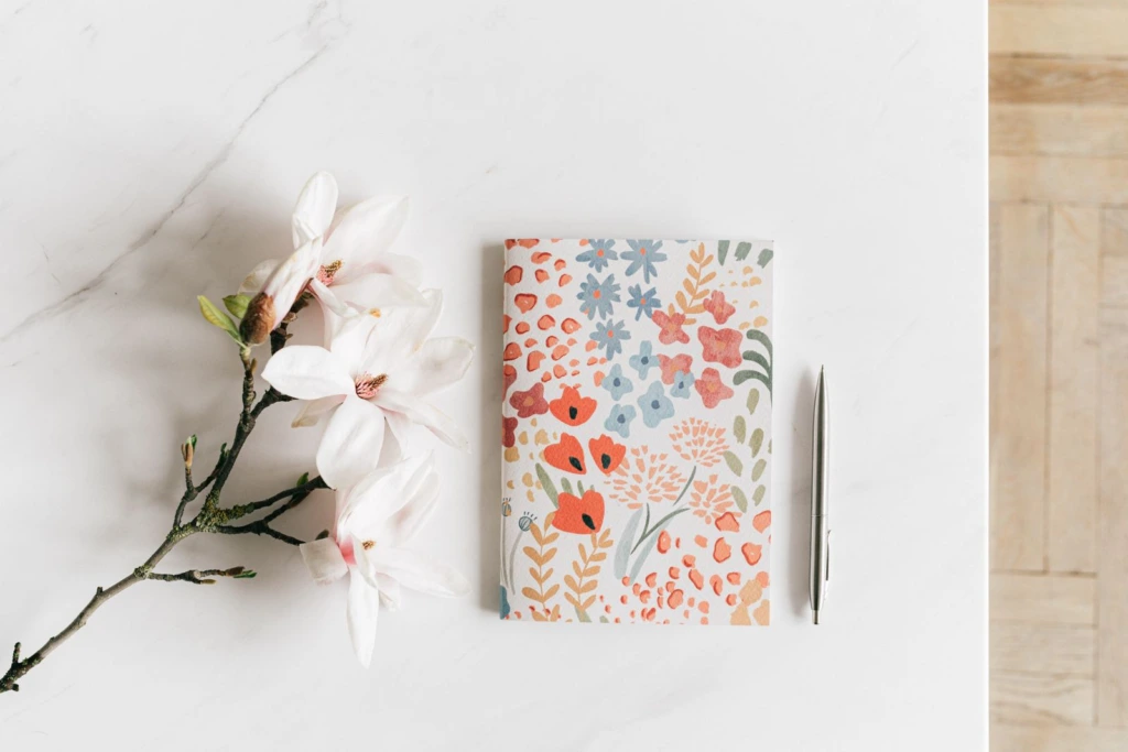 Libreta con flores y pluma junto a una rama de magnolia blanca