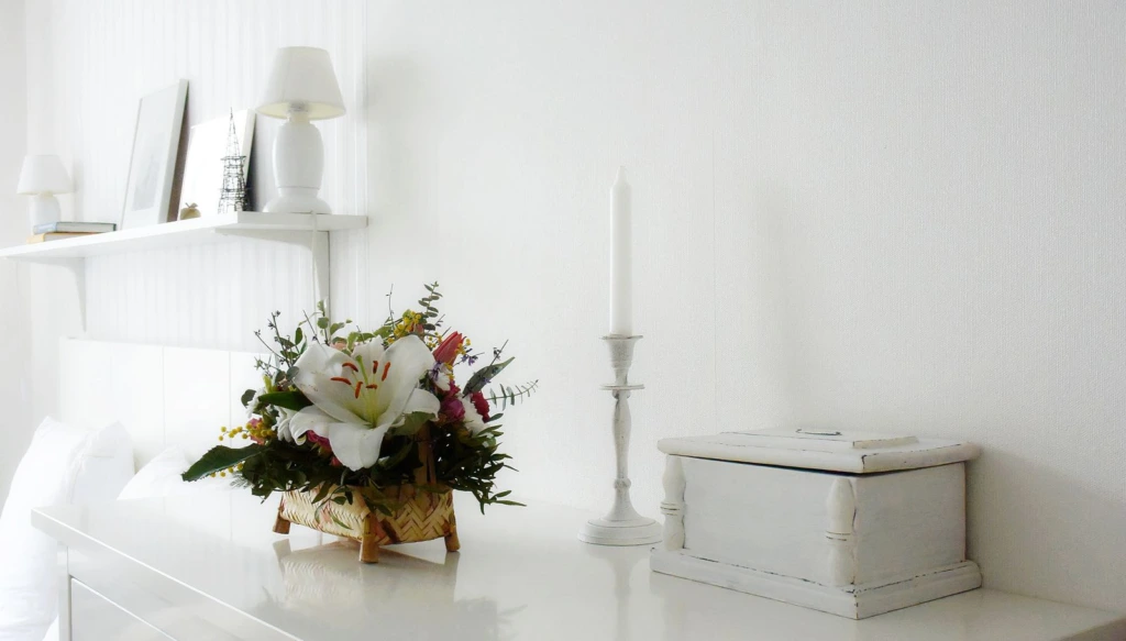 Arreglo de flores blancas junto a un candelero sobre un mueble blanco